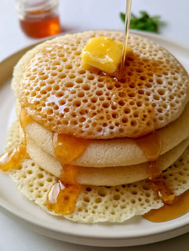 African Crepes: The Ultimate Guide to Moroccan Baghrir Thousand-Hole Pancakes 1 Thick amber honey being poured over a stack of African crepes, filling the porous holes.