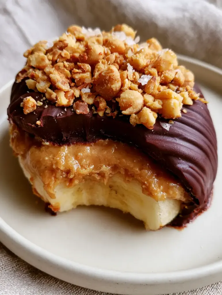 Frozen Banana Snickers: The Ultimate Healthy Bite-Sized Snack 2 Close-up handheld photo of a frozen banana snickers slice with a bite taken out, showing distinct layers of banana, peanut butter, and chocolate shell. (frozen banana snickers)
