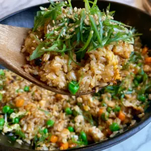 Close-up handheld smartphone photo of long-grain jasmine fried rice with charred chicken and green scallions in a matte black wok. (fried rice recipe)