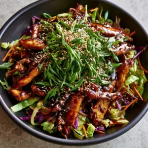 Extreme close-up of seared chicken breast strips coated in a thick, dark hoisin sauce with sesame seeds and scallions. (Moo Shu Chicken)