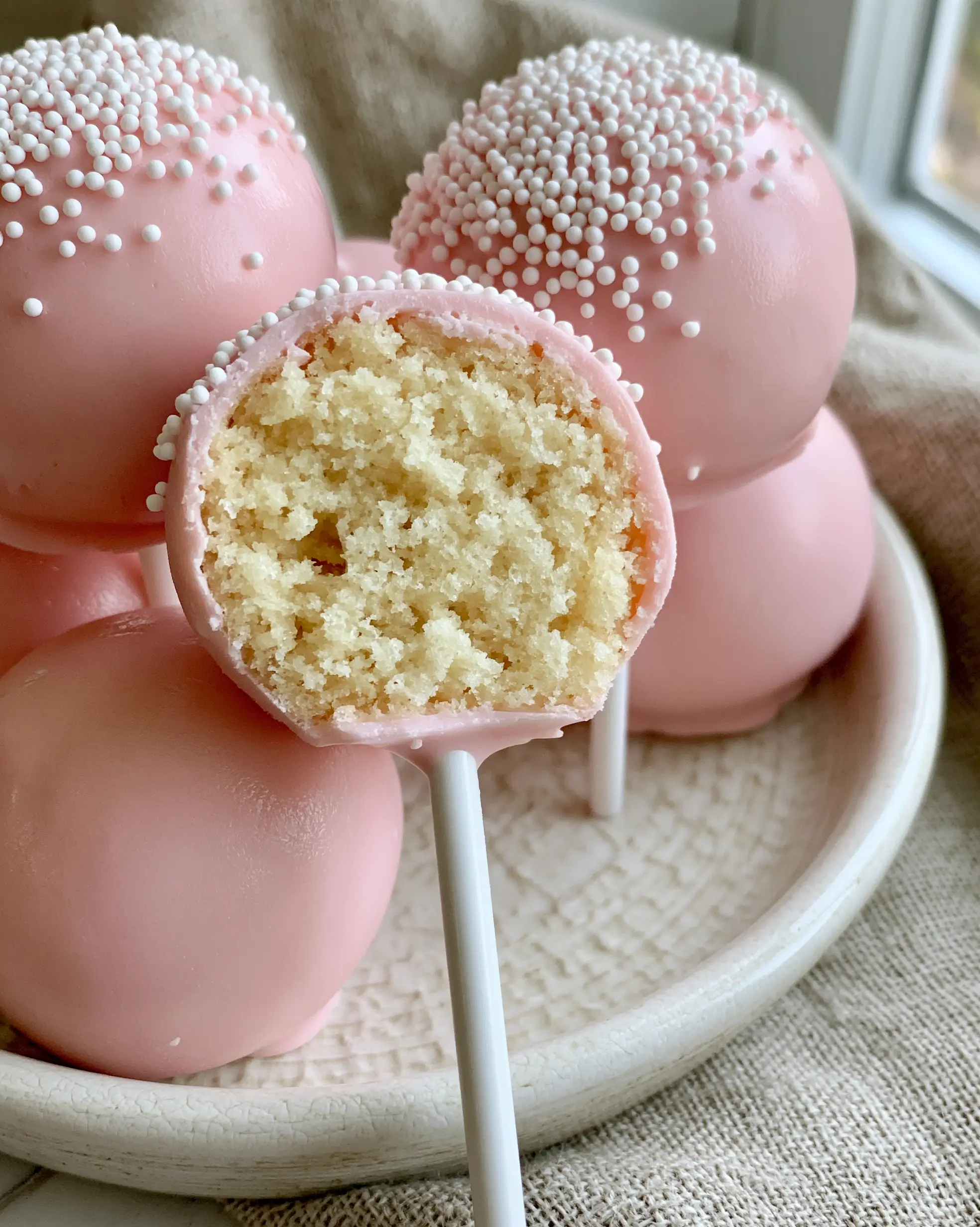 A close-up of copycat pink cake pops showing a clean bite and dense vanilla interior. (cake pop recipes)