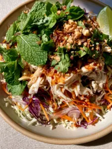 A top-down macro shot showing the glossy amber Nuoc Cham dressing drizzled over hand-shredded chicken and vibrant cabbage. (Vietnamese Chicken Salad)