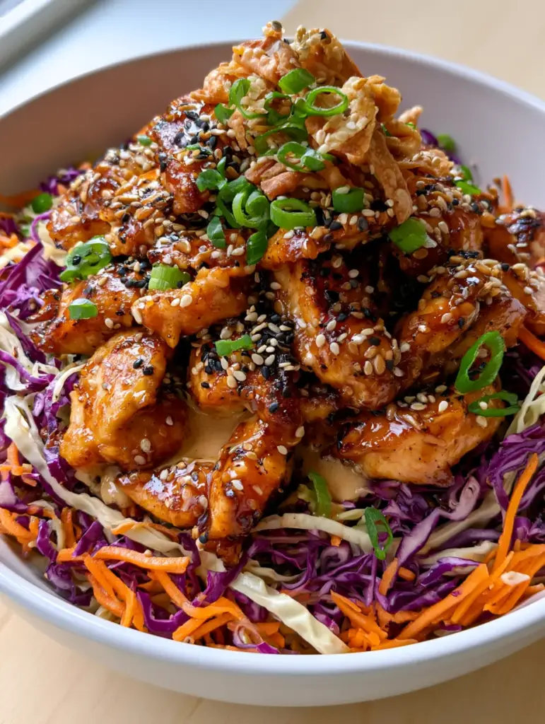 Sesame Chicken Salad with Glossy Ginger Glaze and Creamy Dressing 2 Close up of seared golden-brown chicken bites coated in a thick amber sesame glaze on a bed of cabbage. (sesame chicken salad)