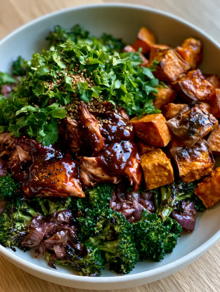 BBQ Chicken Sweet Potato Bowl with Charred Broccoli and Red Onions 2 Close up shot of shredded chicken in a thick mahogany BBQ glaze next to roasted sweet potato cubes. (BBQ chicken sweet potato bowl)