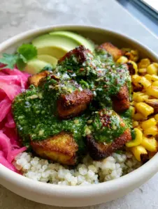 Macro close-up of golden seared tofu cubes drizzled with emerald-green chimichurri sauce in a ceramic bowl. (Vegan Chimichurri Tofu Bowl)
