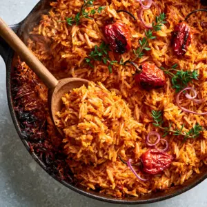 Top-down view of Cameroonian Jollof Rice in a black pot, showing individual long-grain rice coated in spicy tomato oil with steam rising.