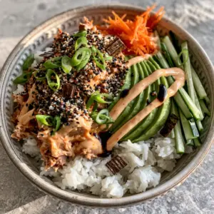 Top-down view of a spicy tuna bowl showing chunky tuna in sriracha mayo, matchstick cucumbers, and fluffy jasmine rice. (spicy tuna bowl)