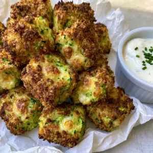 Highly textured zucchini tots with panko crust and visible green flecks on a light wooden table.