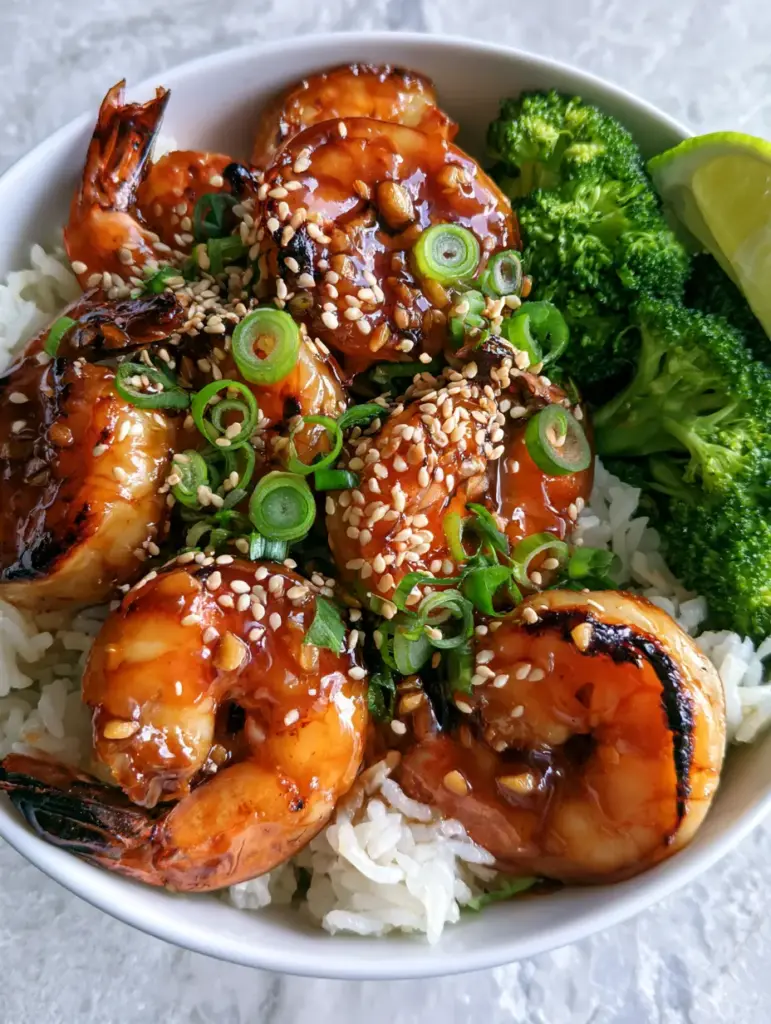 Close up of seared jumbo shrimp with golden-brown charred edges and green scallion garnishes in a bowl.