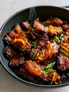 A handheld smartphone photo showing the deeply seared and crispy jagged edges of Sticky Orange Beef in a matte black skillet.