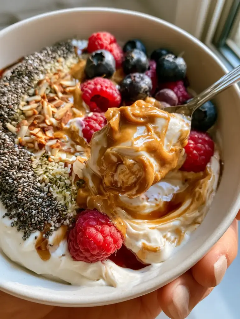 Handheld photo of a luscious yogurt bowl with velvety swirls and glossy almond butter. (no-cook breakfasts)
