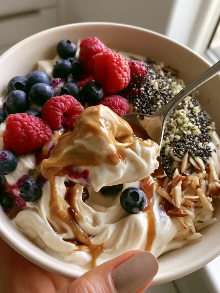 No-Cook Breakfasts: High-Protein Berry & Almond Butter Yogurt Bowl 1 Close-up of a silver spoon scooping thick Greek yogurt with raspberries and chia seeds.
