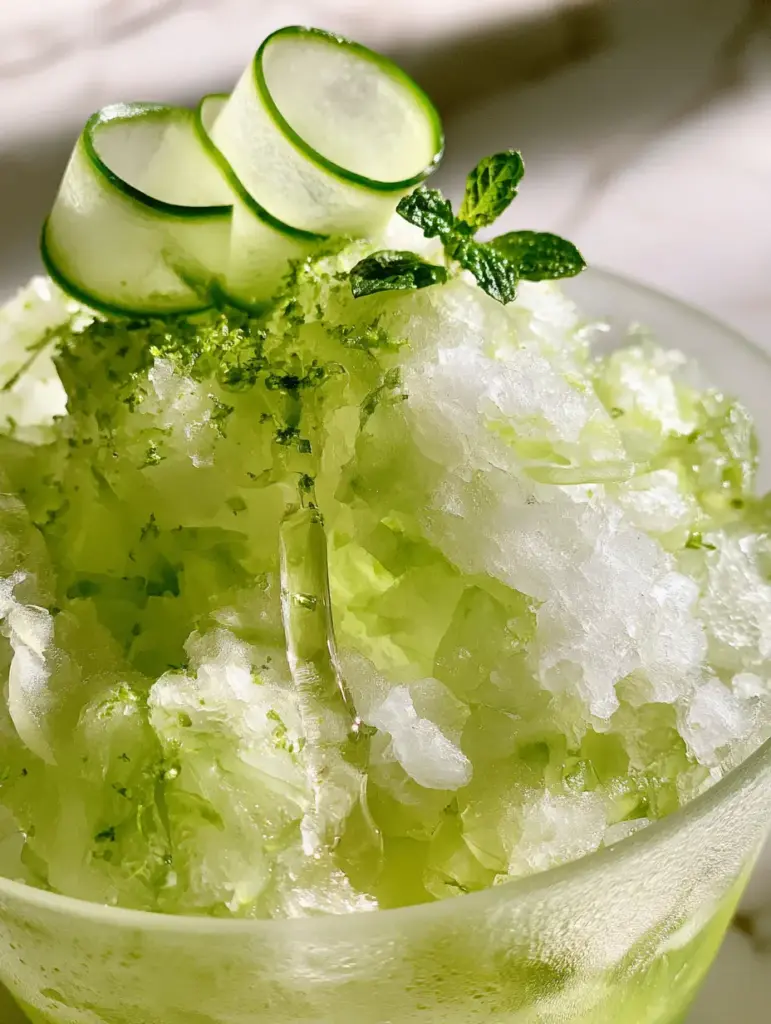A macro shot of fluffy cucumber apple shaved ice showing feathery crystals and lime zest.
