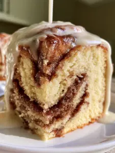 Close up photo of a Cinnabon cinnamon roll cake slice held on a white plate in natural morning light.