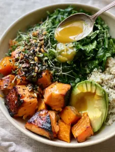 A top-down view of a matte cream bowl filled with charred salmon, orange sweet potato cubes, and green kale. (high protein high fiber dinners)