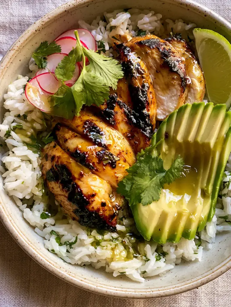 Close up of seared chicken and fanned avocado in a speckled ceramic bowl.