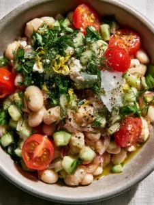Macro photo of glistening cannellini beans, ruby-red cherry tomatoes, and paper-thin red onions in a marinated white bean salad.