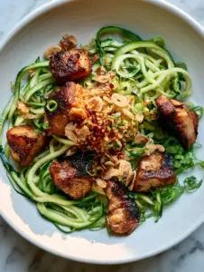Extreme close-up of chicken zucchini noodles stir fry showing caramelized chicken and vibrant green ribbons.