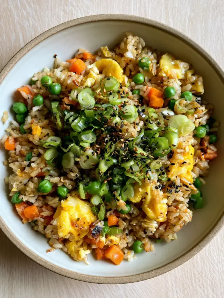Egg Fried Rice with Golden Toasted Grains and Fluffy Egg Ribbons 1 A top-down view of egg fried rice in a minimalist bowl on a light wood surface, highlighted by natural side lighting.