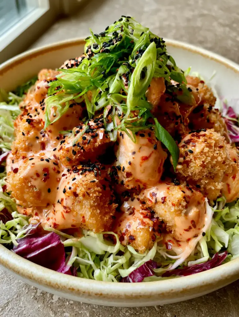 Plated Crispy Bang Bang Chicken in a matte cream ceramic bowl on a stone countertop with warm natural lighting.