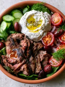Macro shot of seared lamb with charred edges and snow-white dairy-free tzatziki in a Paleo gyro bowl.