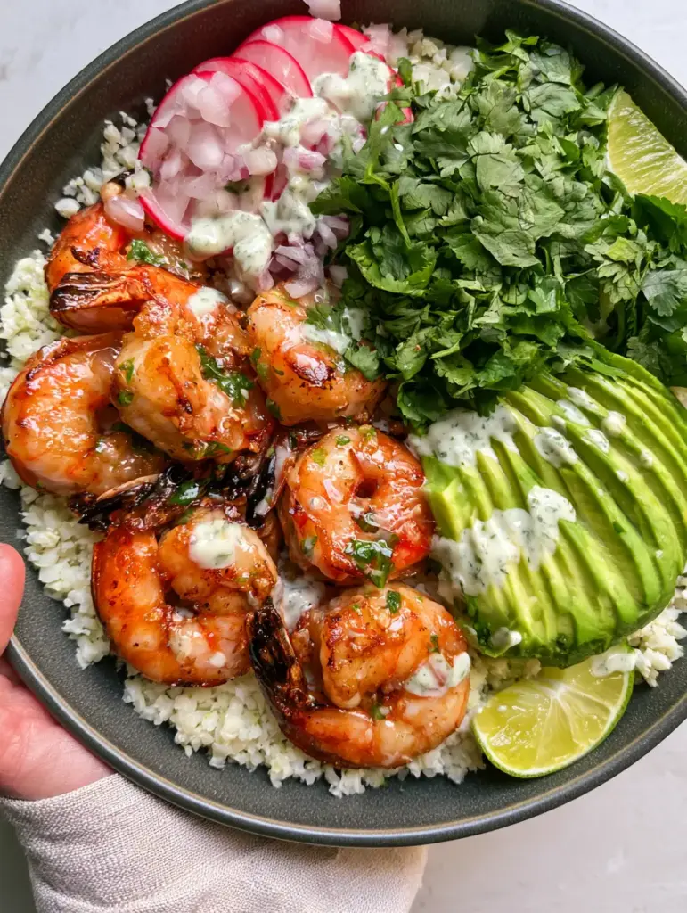 Overhead view of a person holding a charcoal bowl of Shrimp Avocado Bowls with cilantro crema drizzle.