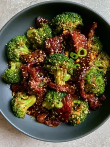 Top-down macro shot of velveted flank steak and emerald broccoli in a mahogany soy-ginger glaze. (beef and broccoli recipe)