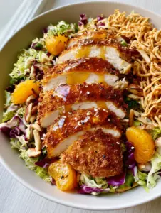 Close up of crispy panko-breaded chicken strips on a bed of shredded green cabbage and purple radicchio, drizzled with amber ginger dressing. (Oriental Chicken Salad)