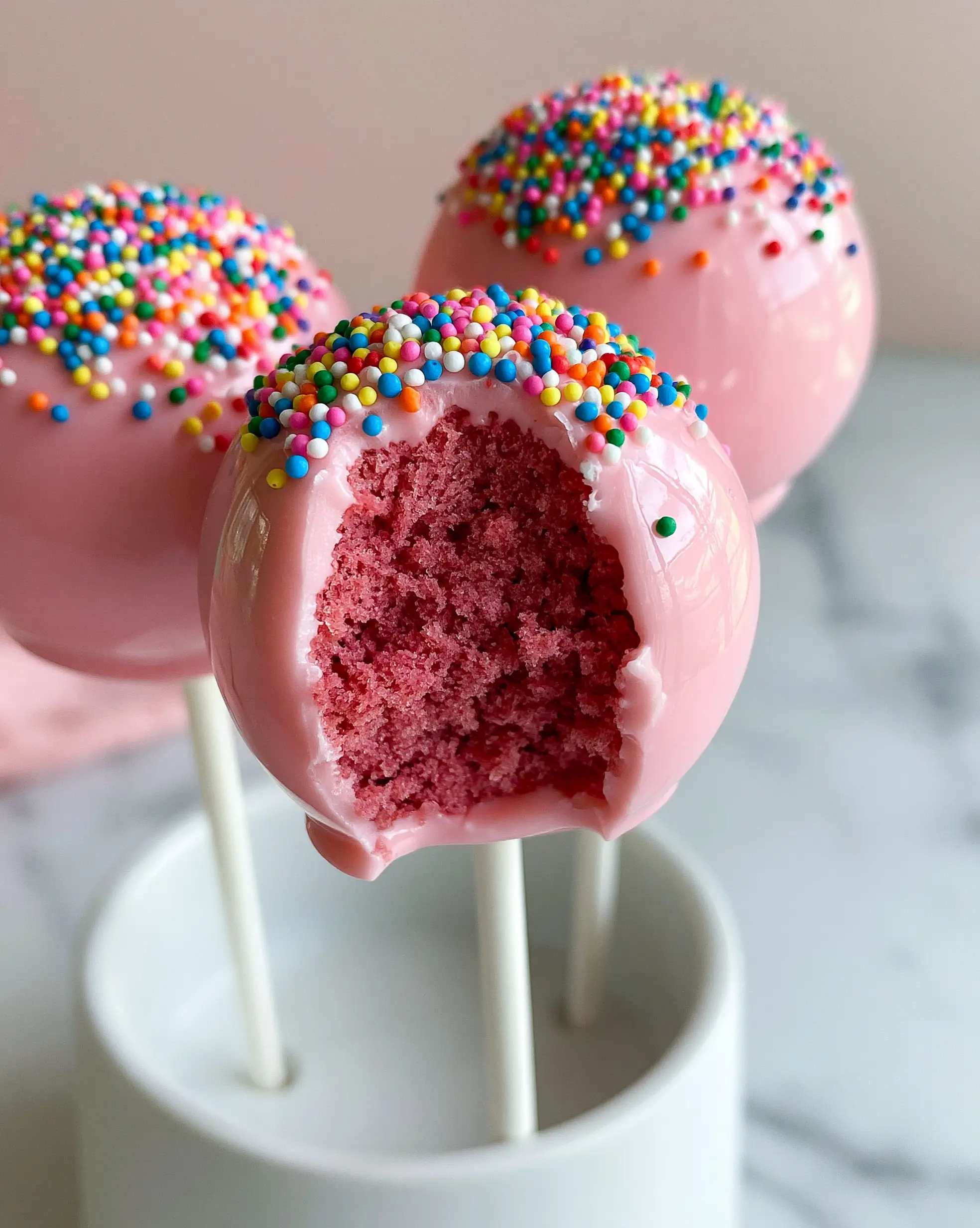Birthday Cake Pops: The Ultimate Guide to Glossy, Vibrant Pink Gourmet Treats 3 Close up handheld photo of Birthday Cake Pops with one showing a moist pink vanilla cake center.
