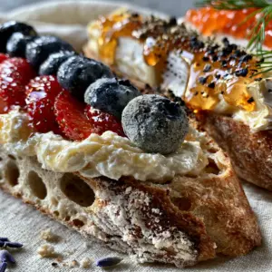 Close-up of a French tartine with whipped honey creme fraiche, sliced strawberries, and blueberries. (Bastille Day recipes)