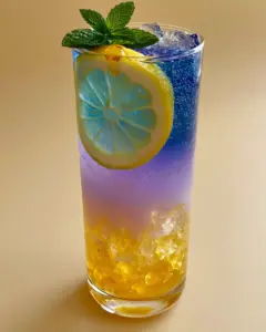 Close up photo of Honey Lemon Butterfly Fizz showing effervescent bubbles and crushed ice layers in a tall glass.