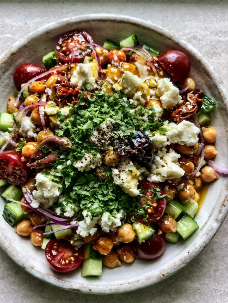 Greek Chickpea Salad: The Ultimate 10-Minute Mediterranean Refresh 2 A handheld smartphone photo of a greek chickpea salad featuring deep red cherry tomatoes and glistening golden vinaigrette.